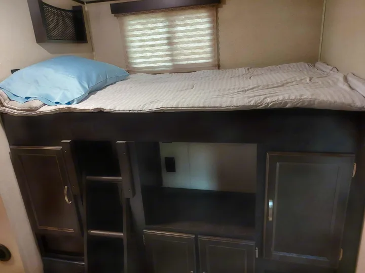 Cozy RV rental bunk bed interior with a striped mattress, blue pillow, window, and built-in storage below.. Coachmen Other 2020