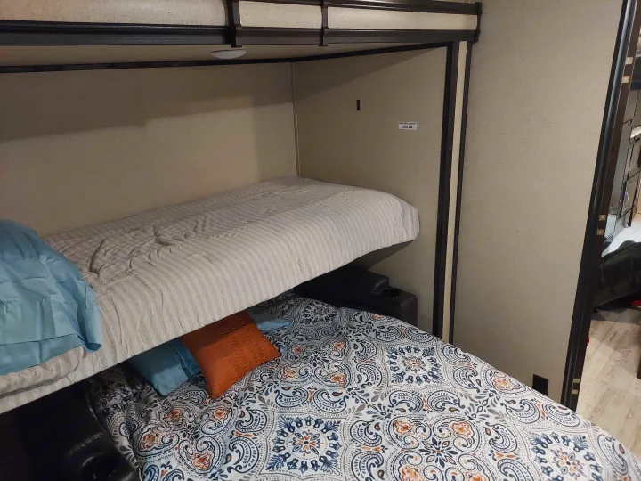 Cozy RV rental bunk beds: top with striped bedding, lower converts to a bed with colorful pattern & cup holders for comfort.. Coachmen Other 2020