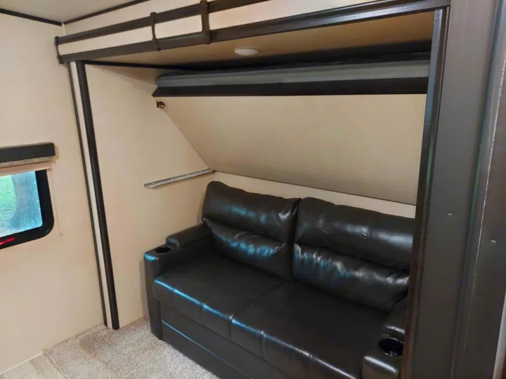 This rv rental features a cozy living area with a dark leather sofa, integrated cup holders, and a clever fold-down bunk.. Coachmen Other 2020