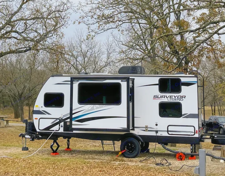 RV rental parked at a serene campsite, a white Surveyor Legend travel trailer nestled among trees.. Forest River Surveyor Legend 2022