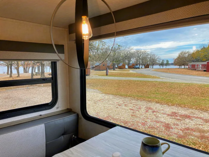 Cozy RV rental interior with a view of lakeside cabins and fall foliage at a campground. Perfect for a nature getaway.. Forest River Surveyor Legend 2022