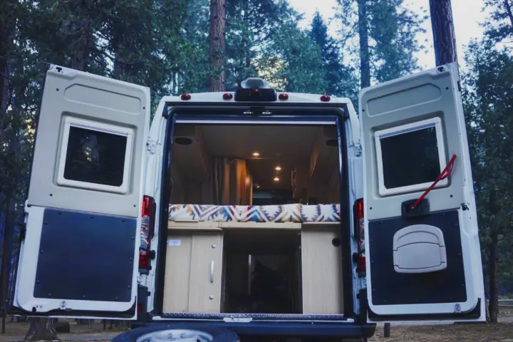RV rental: Camper van's open rear doors showcase a cozy interior with a bed & storage, parked in the woods.. Hymer Hymer Class B 2019
