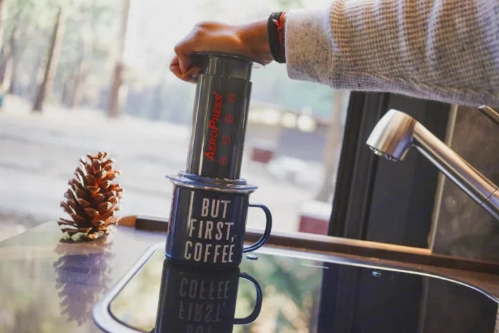 Making coffee with an AeroPress and 'BUT FIRST, COFFEE' mug in an RV rental kitchen, with a pinecone and sink.. Hymer Hymer Class B 2019