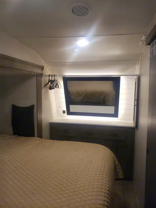 Explore this modern RV rental bedroom featuring a comfy bed, built-in storage, and illuminated vanity mirror.. Forest River Shockwave 2021
