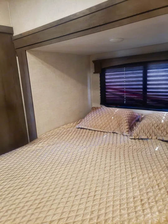 Inside a modern RV rental, this bedroom offers a quilted bed, window with blinds, and light, inviting decor for comfortable stays.. Forest River Shockwave 2021