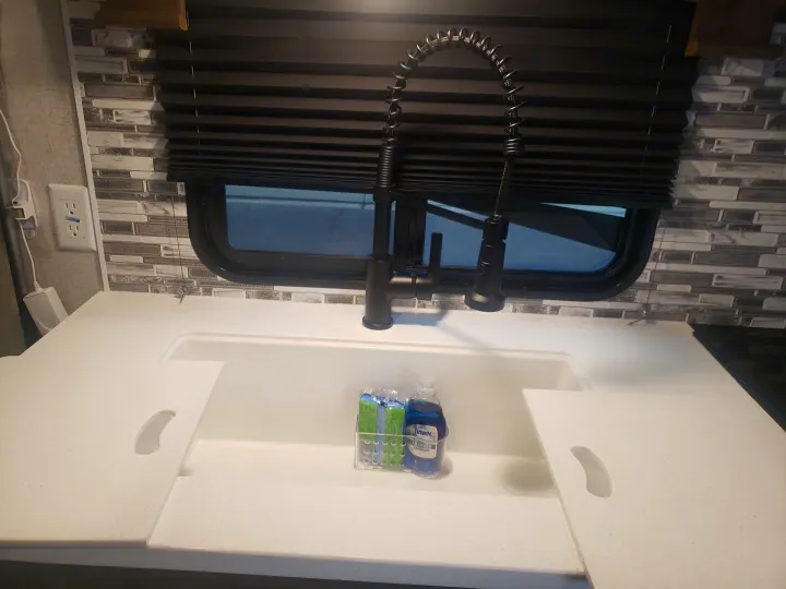RV rental kitchen: modern black pull-down faucet, spacious white sink, speckled countertops, and tiled backsplash.. Forest River Shockwave 2021