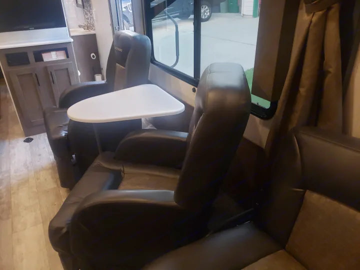 Comfortable RV rental interior showing two black recliners with an attached side table, wood-look floor, and window view.. Forest River Shockwave 2021