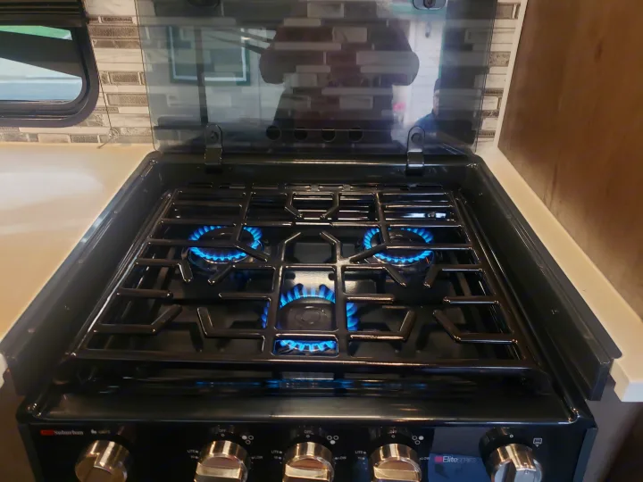 Clean, modern three-burner gas stove, with all burners active showing blue flames, ready for your RV rental adventure.. Forest River Shockwave 2021