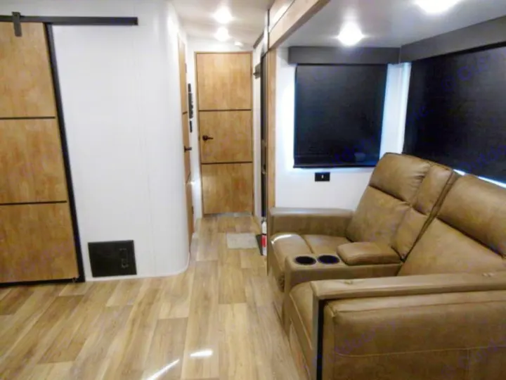Step inside this RV rental's cozy interior, showcasing a brown reclining sofa, wood-look floor, and modern wood paneled doors.. Keystone Outback 340 BH 2022