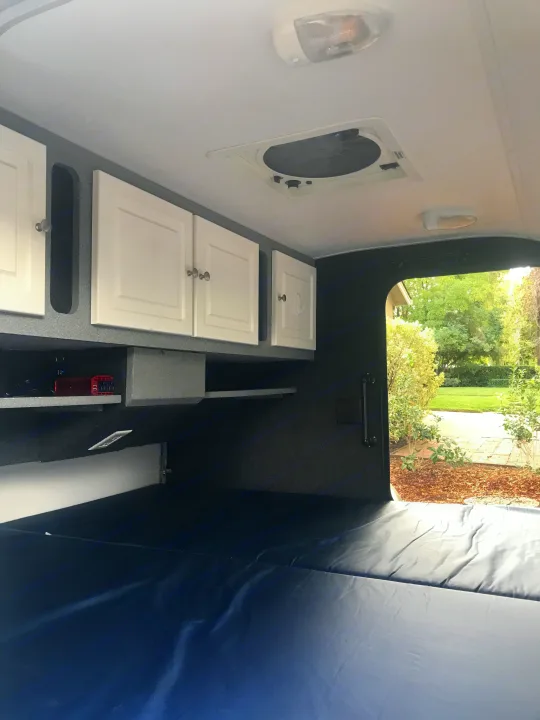 Spacious RV rental interior with white overhead storage, a blue bed, ceiling fan, and outdoor view from the rear.. Little Guy Other 2011