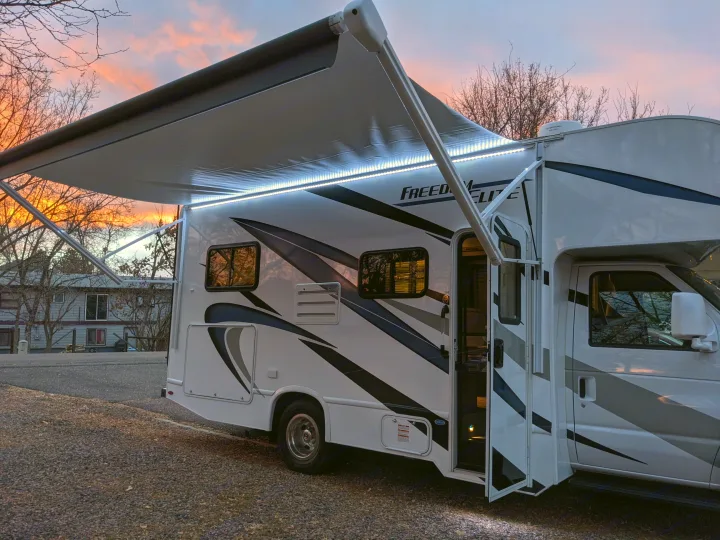 RV rental with illuminated awning at sunset. Perfect for camping and travel adventures.. Thor Freedom Elite 2021