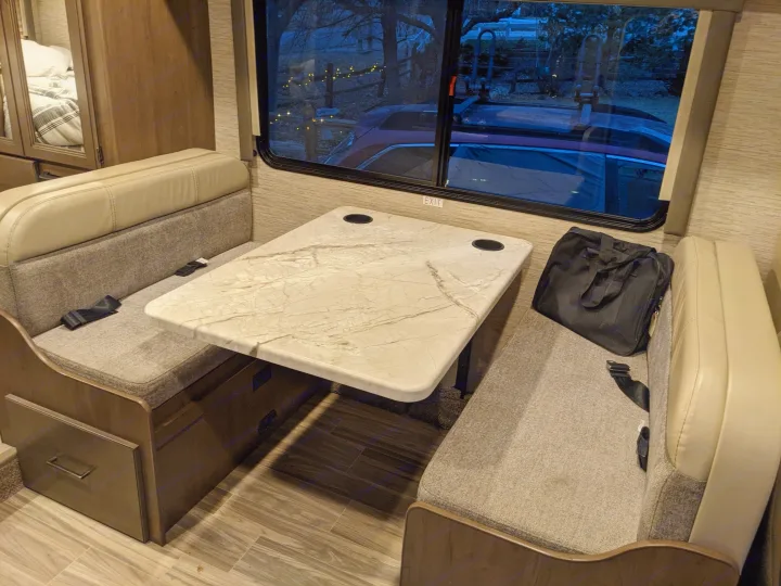 Cozy RV rental dinette with marble-look table, comfortable benches, and scenic window view of the outdoors.. Thor Freedom Elite 2021