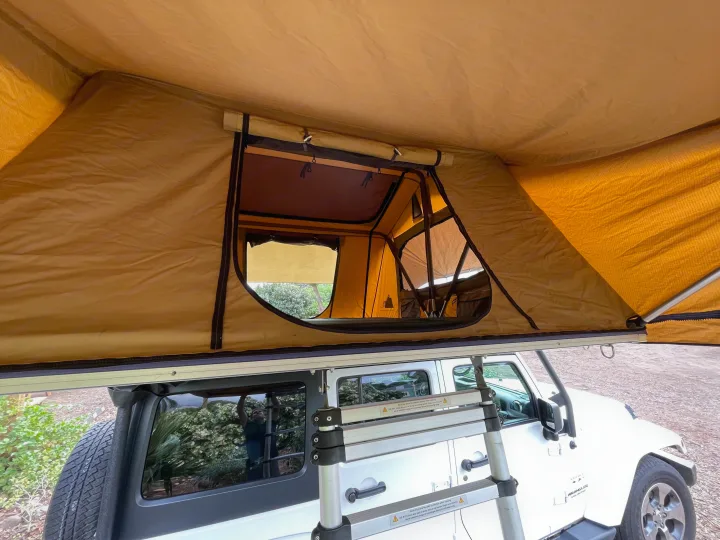 View from below an open rooftop tent on a white Jeep Wrangler, an agile RV rental alternative for overland camping adventures.. Jeep Wrangler 2017