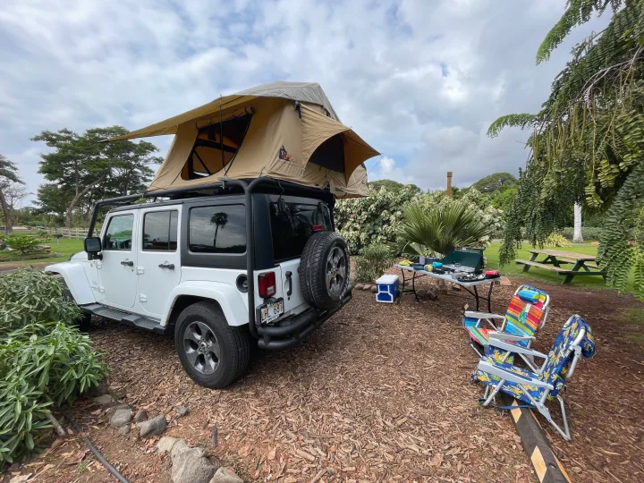 White Jeep Wrangler with a rooftop tent at a campsite, offering an RV rental alternative for comfortable outdoor adventures.. Jeep Wrangler 2017