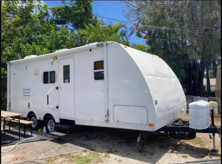 White travel trailer RV rental, parked in a sunny campsite. Features an outdoor picnic table. Perfect for trips.. Heartland North Trail 2009