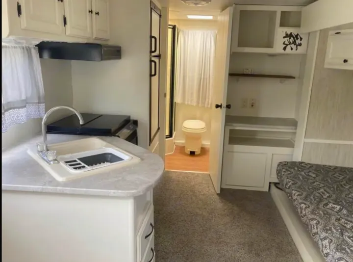 View of an RV rental's interior, showcasing its kitchen, bathroom with toilet, and bedroom with a patterned bed.. Heartland North Trail 2009
