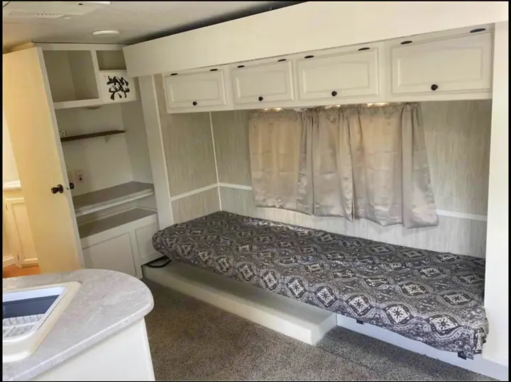 Inside this rv rental: a cozy single bed, overhead storage cabinets, shelves, and a kitchen counter. Perfect for travel.. Heartland North Trail 2009