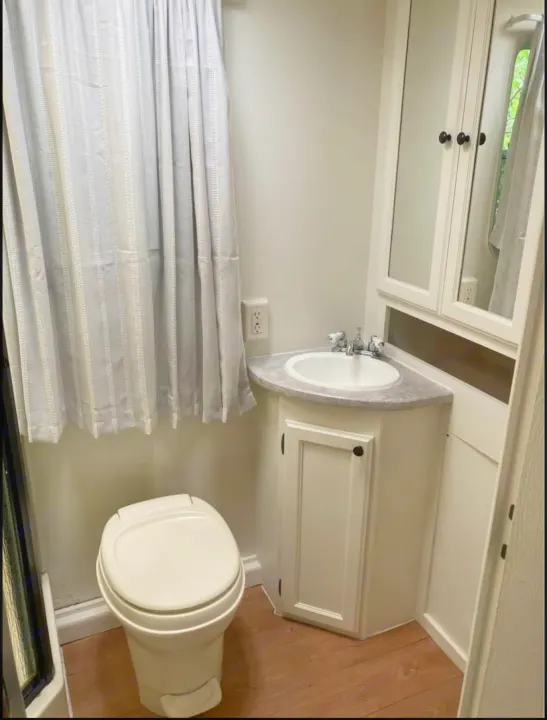 Compact RV rental bathroom: white toilet, corner sink, and striped shower curtain. Clean and functional.. Heartland North Trail 2009