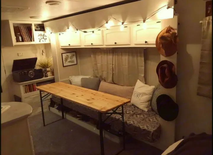 Cozy RV rental interior: wooden table, cushioned seating, white overhead cabinets with string lights, and a record player.. Heartland North Trail 2009