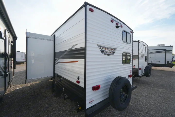 White toy hauler RV rental with an open rear ramp door, parked with other travel trailers on a gravel lot.. Wildwood FSX 178BHsk 2022