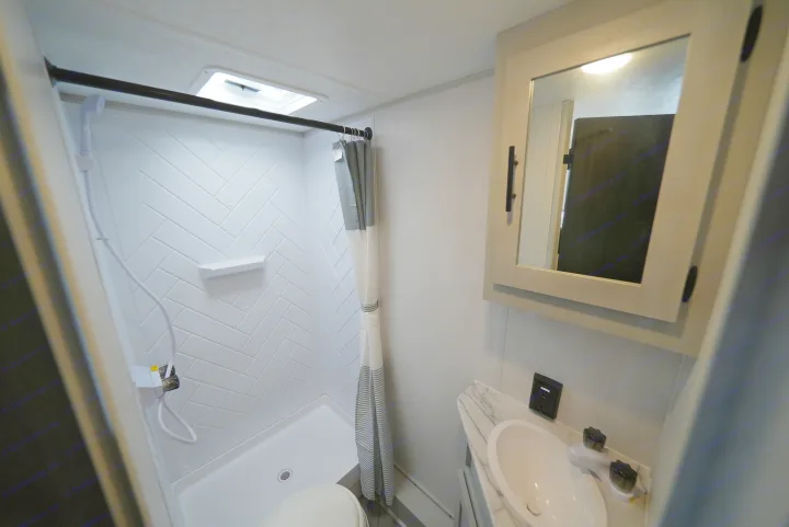 RV rental bathroom: Clean and compact with a herringbone-tiled shower, toilet, and vanity sink with mirror.. Wildwood FSX 178BHsk 2022