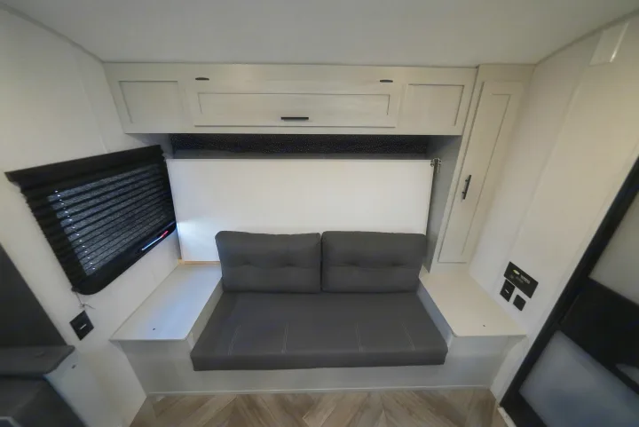 RV rental interior featuring a gray sofa, overhead cabinets, and a fold-down bed/table. Compact and functional space.. Wildwood FSX 178BHsk 2022