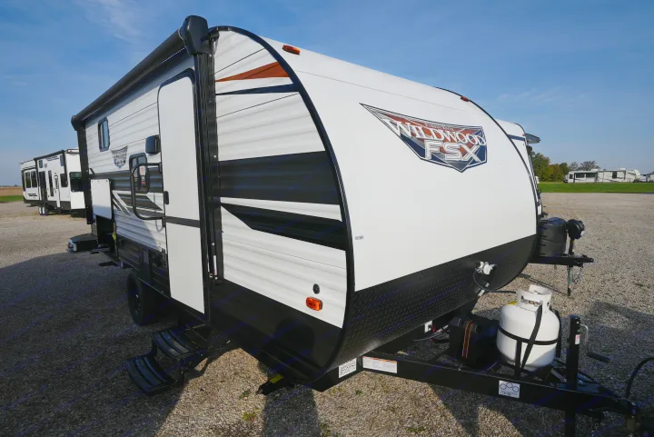 A pristine white & black Wildwood FSX travel trailer, ideal for an rv rental, sits on a gravel lot under blue sky.. Wildwood FSX 178BHsk 2022