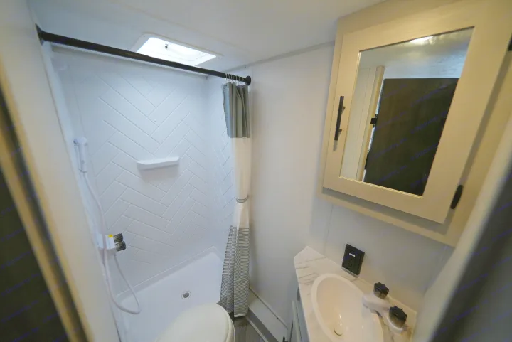 Compact RV rental bathroom with shower, toilet, and vanity. Features herringbone shower walls, sink, and skylight.. Wildwood FSX 178BHSK 2022