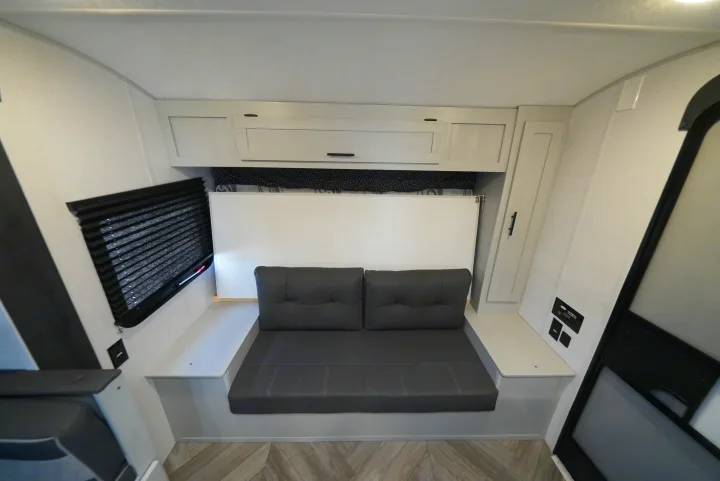 Compact RV rental interior featuring a gray convertible sofa/bed, white overhead cabinets, and window.. Wildwood FSX 178BHSK 2022