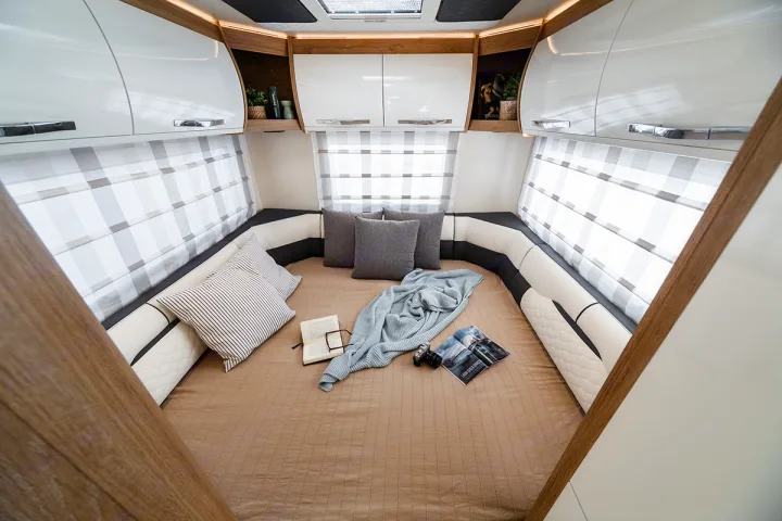 Cozy RV rental interior: a spacious U-shaped bed/seating area with overhead cabinets and window blinds.. Ford Rollerteam 747 2026