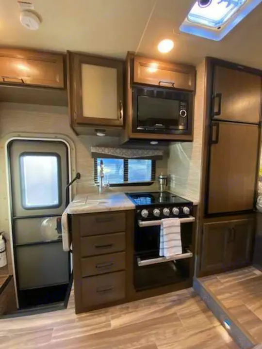 This RV rental features a full kitchen with an oven, microwave, refrigerator, and sink, designed for compact living.. Thor Freedom Elite 2021