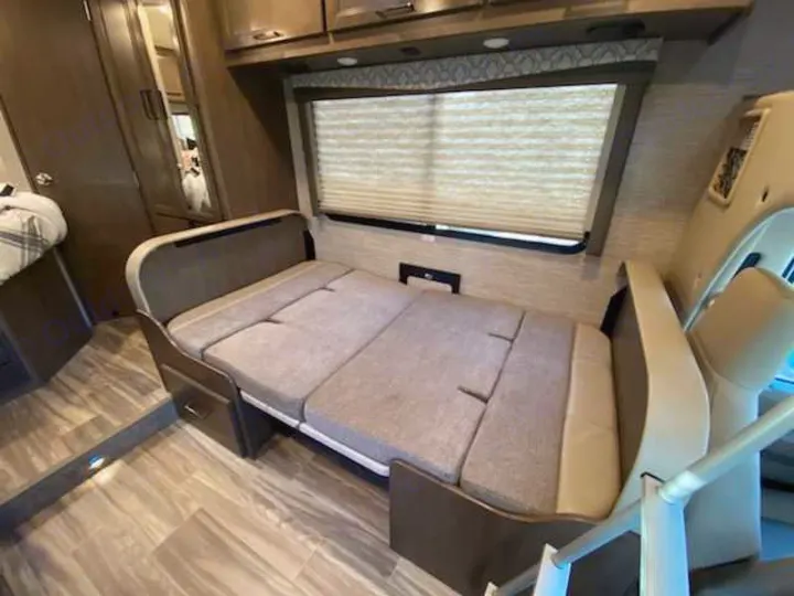 RV rental interior shows a cozy convertible sofa bed, window with blinds, and overhead storage cabinets.. Thor Freedom Elite 2021