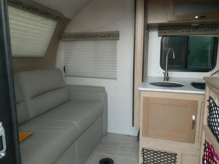 RV rental interior showcasing a comfortable grey sofa, compact kitchen area with a sink, and multiple windows with blinds.. Forest River R-Pod 2020