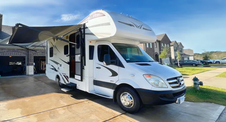 This white Class C RV rental, with awning extended, is parked on a sunny driveway, ready for adventure.. Winnebago Mercedes 2012