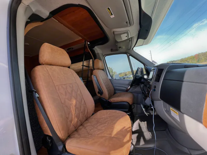 Inside an RV rental: stylish tan leather diamond-stitched seats, overhead storage, and a ladder to the living area.. Winnebago Mercedes 2012