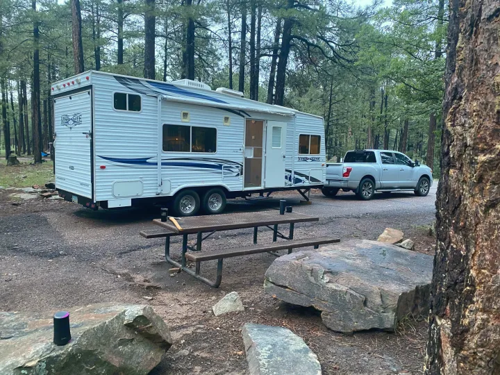 RV rental travel trailer & pickup truck camping in a pine forest campground with a picnic table & speaker.. Rage'N Toy Hauler 2006