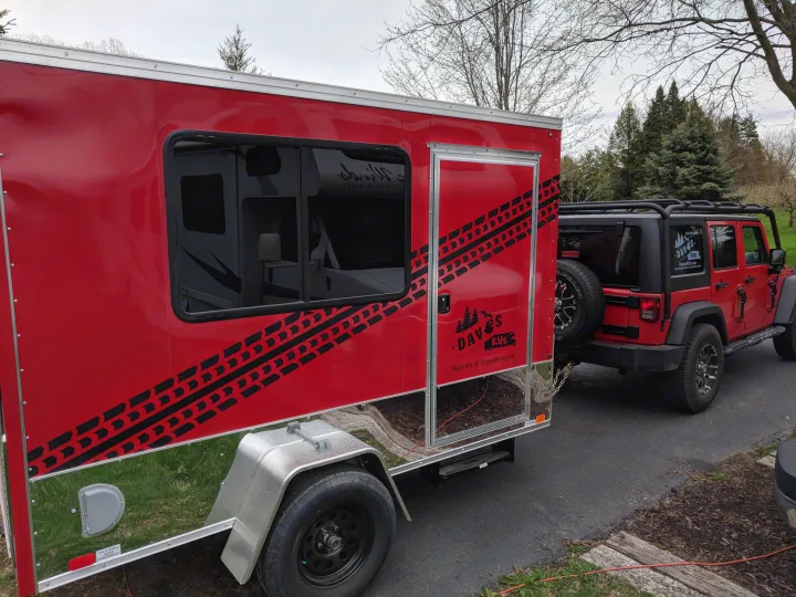 A vibrant red Dave's RVs rental trailer with bold tire track graphics, hitched to a matching red Jeep.. United XLMTV-610 2018