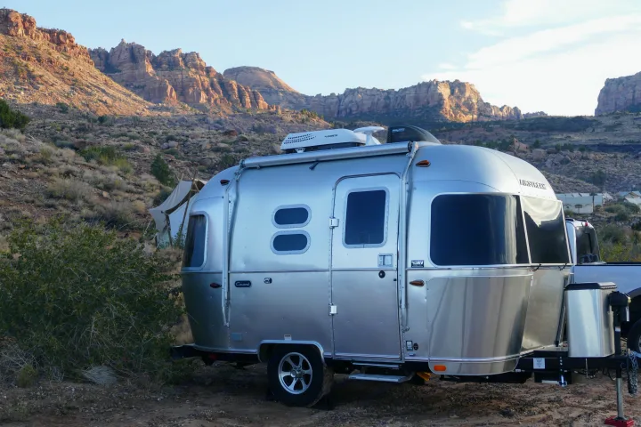 Silver Airstream RV rental parked in a scenic desert landscape with towering rocky mountains and other glamping tents.. Airstream Caravel 2020