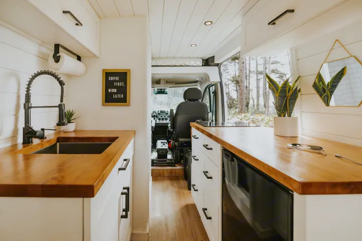 Bright rv rental interior: modern kitchen with wood counters, white cabinets, and living area with plant and mirror.. Ram Promaster 2500 2021