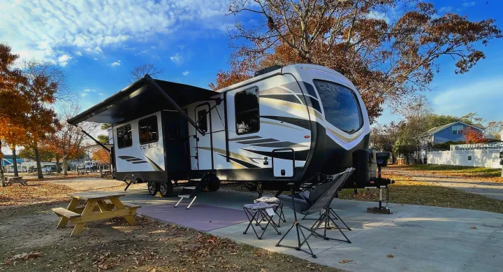 Enjoy your RV rental! This Outback travel trailer is set up with an awning, picnic table, and chairs at a sunny campground.. Keystone RV Outback 2021