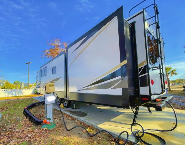 A spacious RV rental is fully set up at a sunny campsite, showcasing power and sewer hookups for a comfortable stay.. Keystone RV Outback 2021