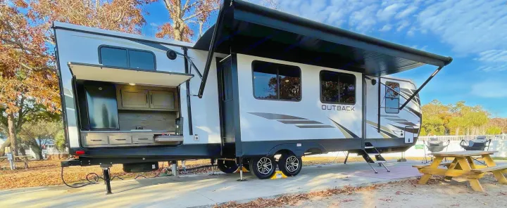 Spacious travel trailer RV rental with outdoor kitchen, extended awning, and picnic area for comfortable camping.. Keystone RV Outback 2021