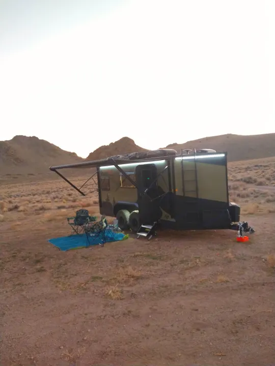 Off-road RV rental trailer with awning & camping setup on dirt in rugged desert terrain, ready for adventure.. Xplorer X22 2022