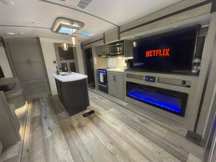 Spacious, modern RV rental interior featuring a kitchen island, entertainment center with Netflix TV & electric fireplace.. Keystone RV Outback 2021