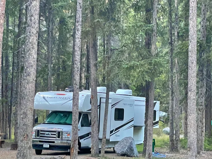 A white Freelander rv rental is parked among tall trees at a peaceful forest campsite, ready for a nature getaway.. Forest River Coachmen Freelander 2021