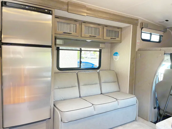 Spacious RV rental interior with a stainless fridge, comfy sofa, window view, and overhead cabinets.. Forest River Coachmen Freelander 2021