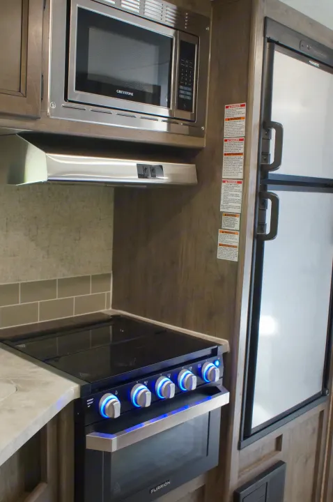 This RV rental kitchen features a Greystone microwave, Furrion stove with blue-lit knobs, and a Dometic refrigerator.. Apex Nano 245 BHS 2020