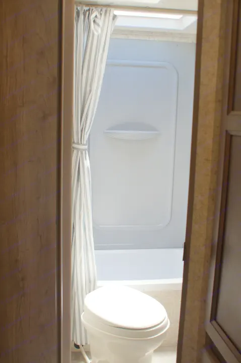 Compact RV rental bathroom features a white toilet, bathtub/shower with gray-and-white striped curtain, and skylight above.. Apex Nano 245 BHS 2020