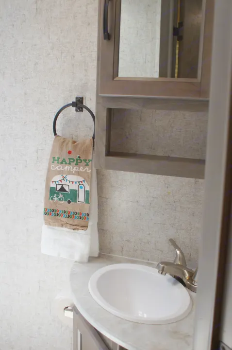 Inside an RV rental: a compact bathroom featuring a sink, mirrored cabinet, and "Happy Camper" towel.. Apex Nano 245 BHS 2020
