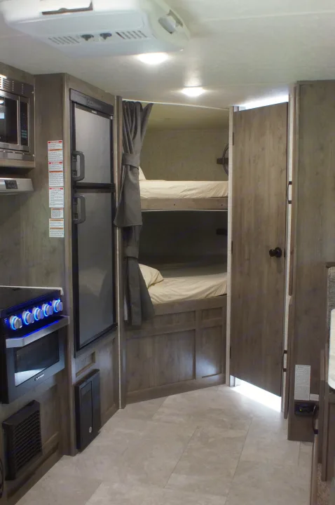 RV rental interior. Kitchenette with microwave, fridge, and stove. Bunk bed area visible with curtains. Tiled floor and ceiling AC unit.. Apex Nano 245 BHS 2020